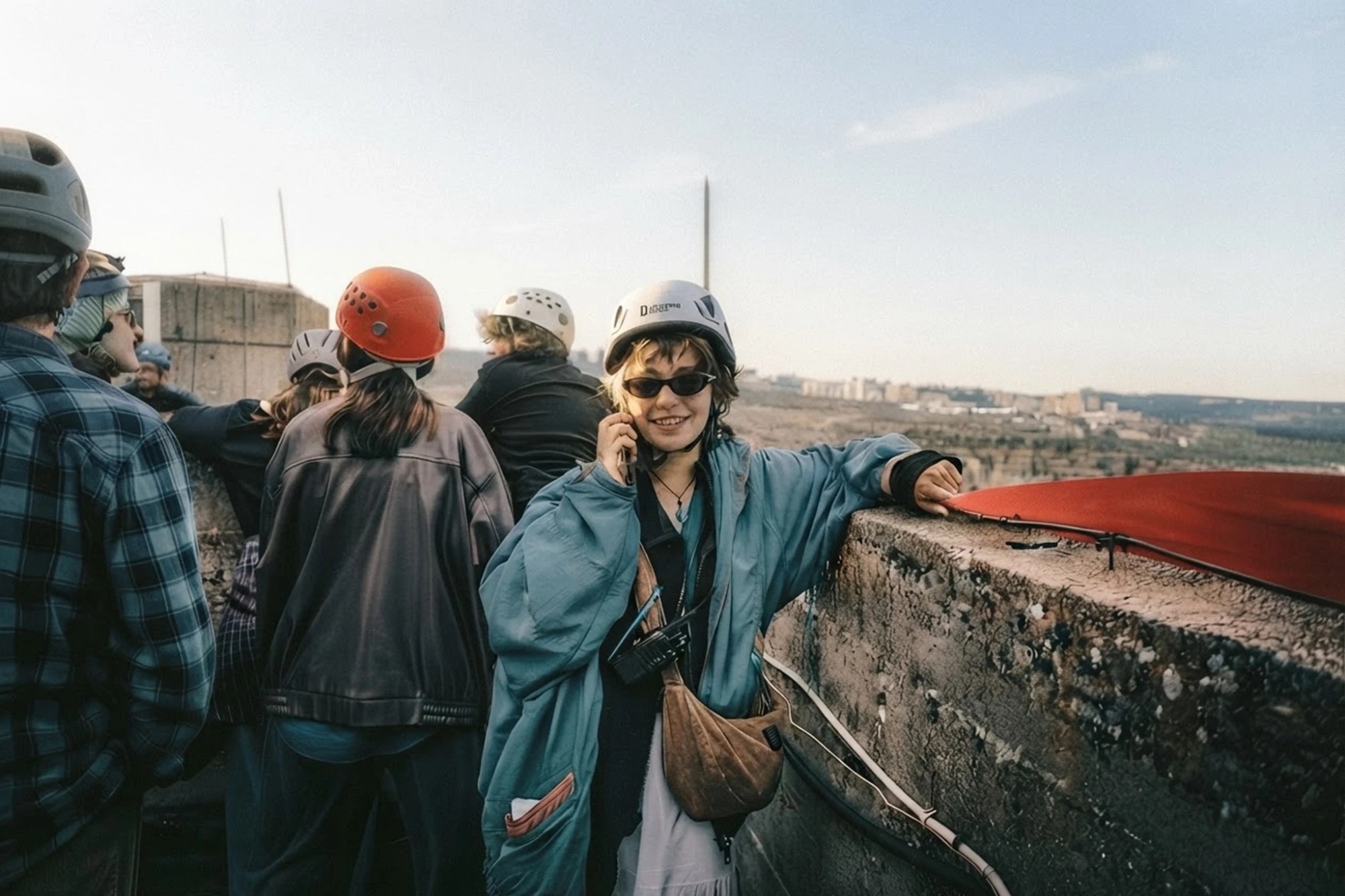 A smiling guide in a climbing helmet on the phone, leading a group on a sunny rooftop