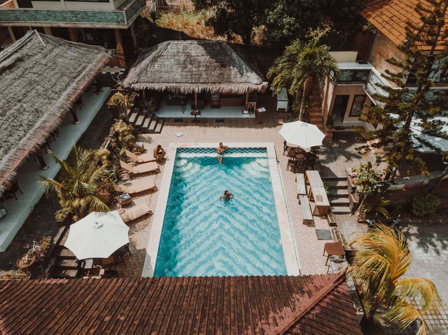 Aerial view of a small guesthouse pool surrounded by thatched roofs and palm trees